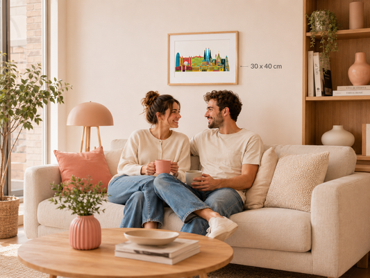 A couple sits on a couch in a cozy living room, smiling and holding drinks, with a framed cityscape artwork hanging on the wall behind them.