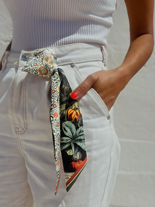 A person wearing a white top and white pants with a colorful scarf tied around their waist.