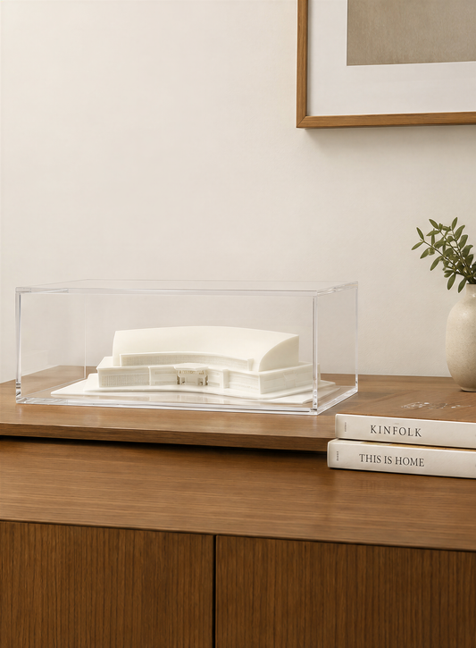 a wooden dresser with a clear glass display case containing a white model of a building, a framed picture, and a stack of books.