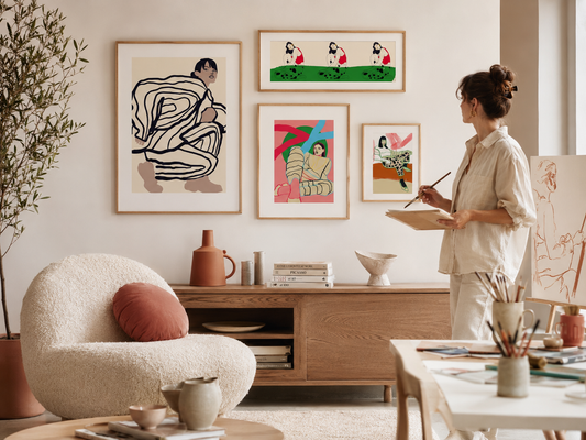 A woman is standing in a room with various artworks displayed on the walls, including abstract paintings and a portrait. She is holding a paintbrush and appears to be engaged in painting or creating art.