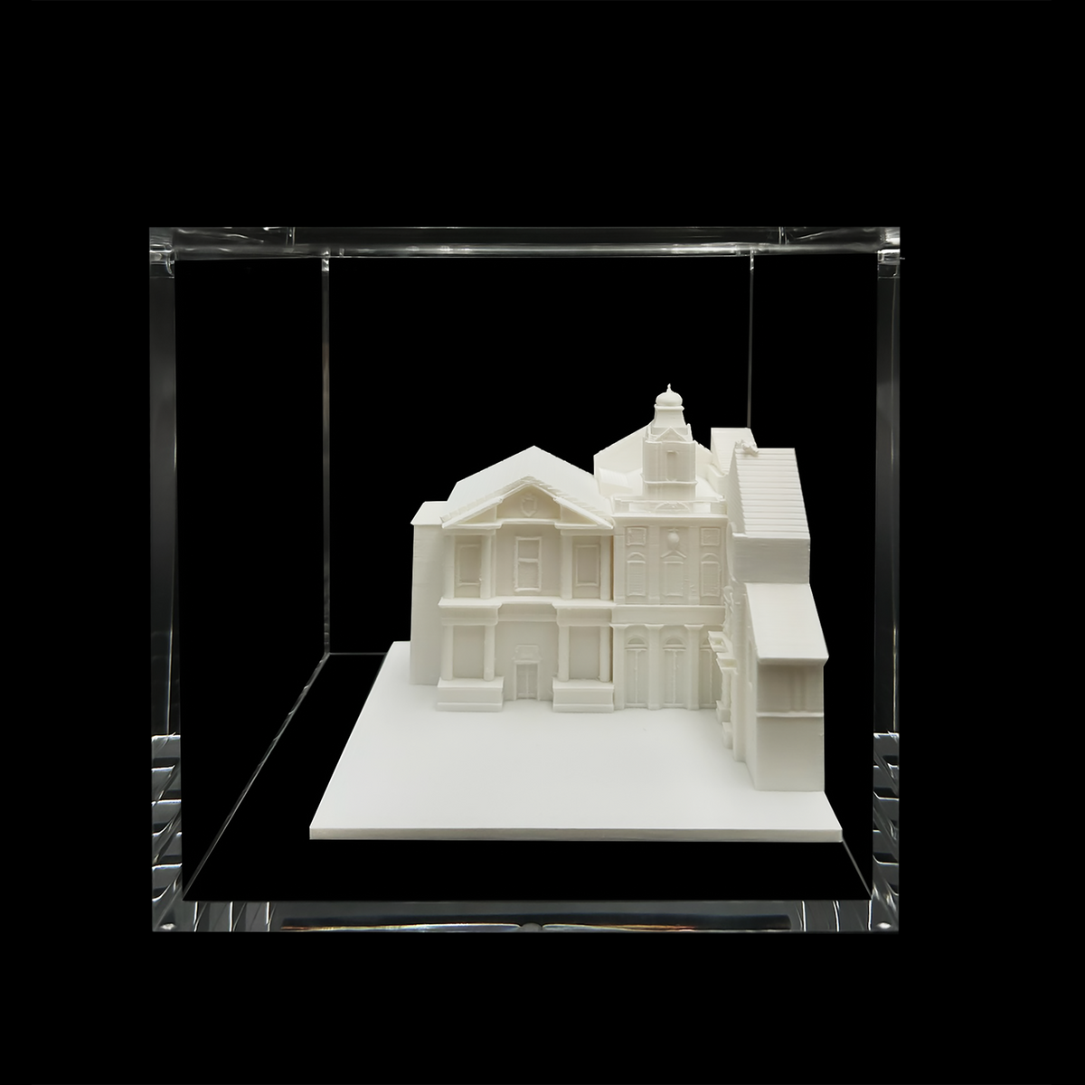 A white 3D model of a building displayed in a clear glass case against a black background.
