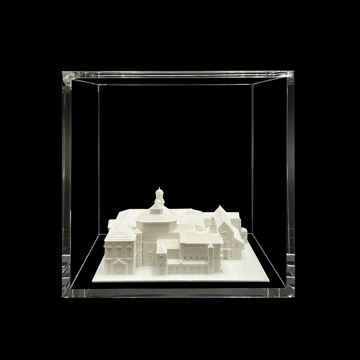 A white 3D model of a building is displayed in a clear glass case against a black background.