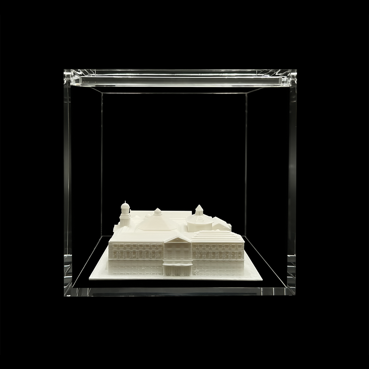 A white 3D model of a building is displayed in a clear glass case against a black background.