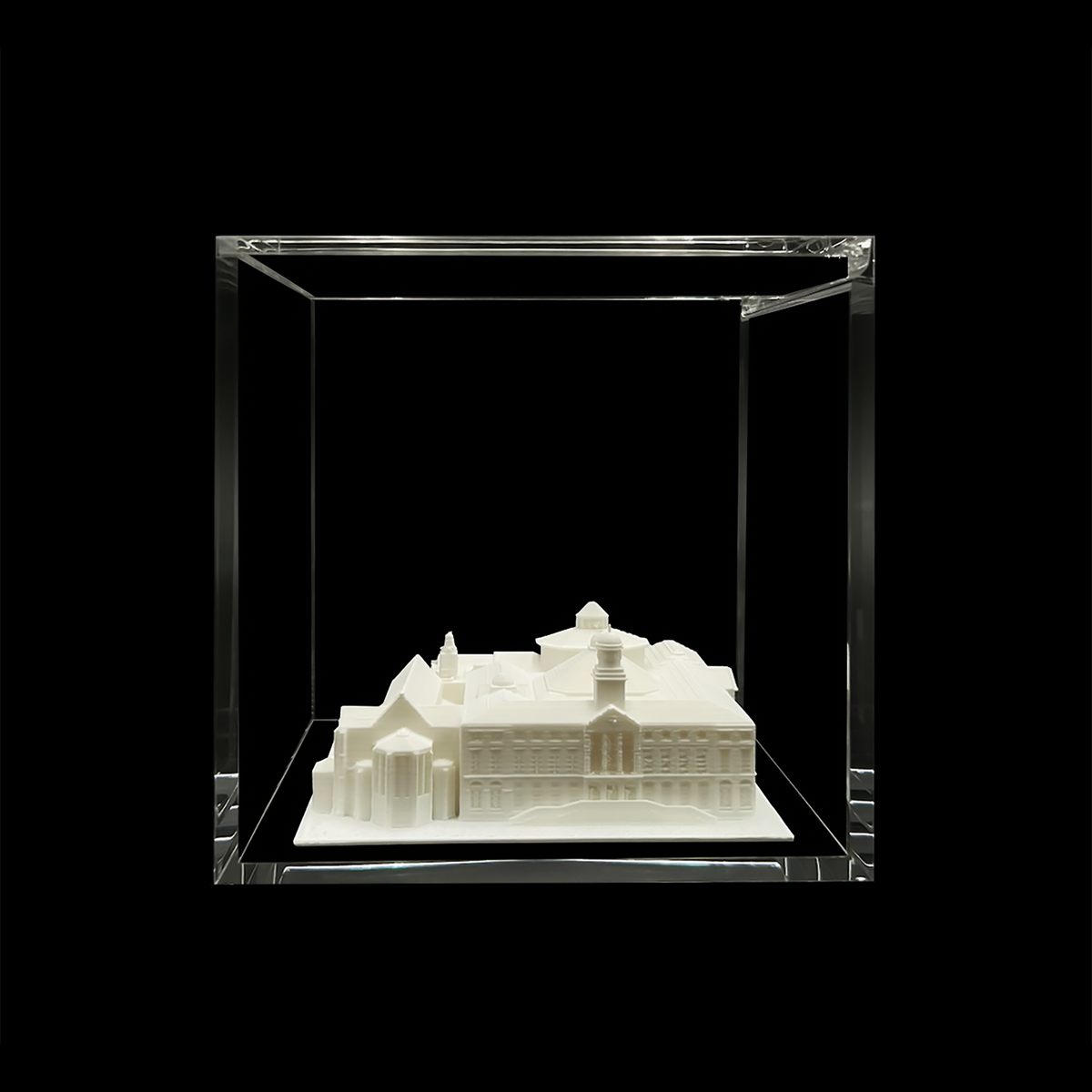 A white 3D model of a building is displayed in a clear glass case against a black background.