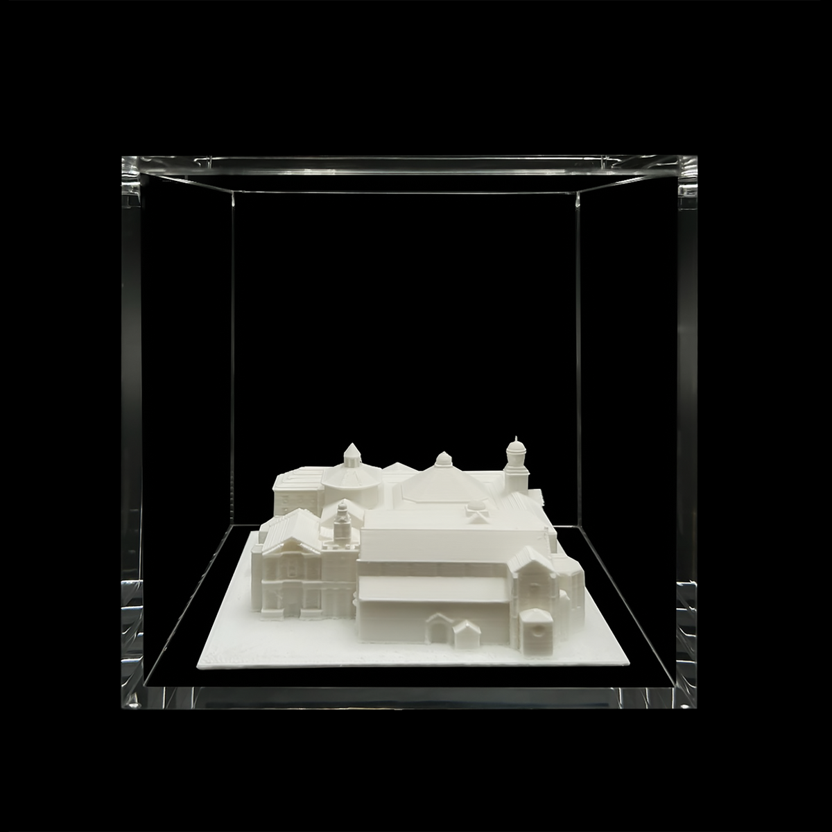 A white 3D model of a building is displayed in a clear glass case against a black background.
