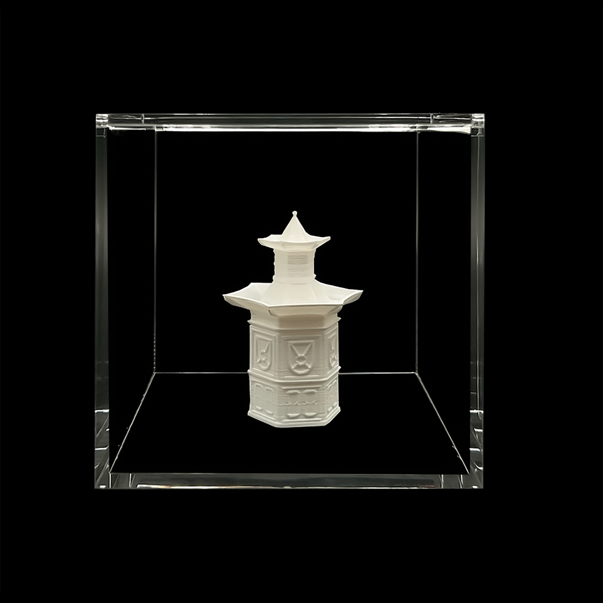 A white ceramic object, possibly a vase or sculpture, is displayed in a clear glass case against a black background.