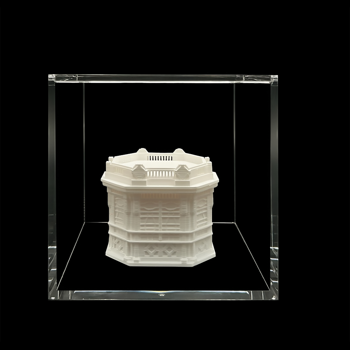 A white, three-dimensional model of a building or structure displayed in a clear glass case against a black background.