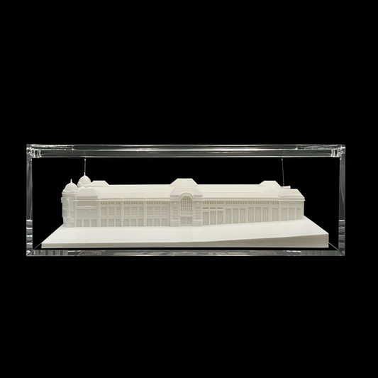 A white architectural model of a building displayed in a clear glass case against a black background.