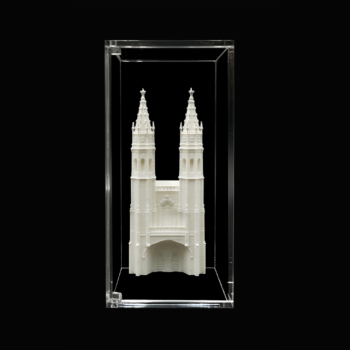 A white 3D model of a cathedral or church with two tall towers, displayed in a clear glass case against a black background.
