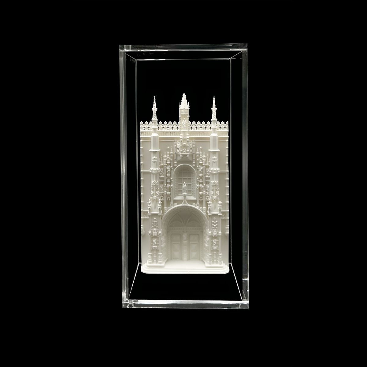 A white, ornate, and intricately designed miniature model of a building, possibly a castle or cathedral, displayed in a clear glass case against a black background.