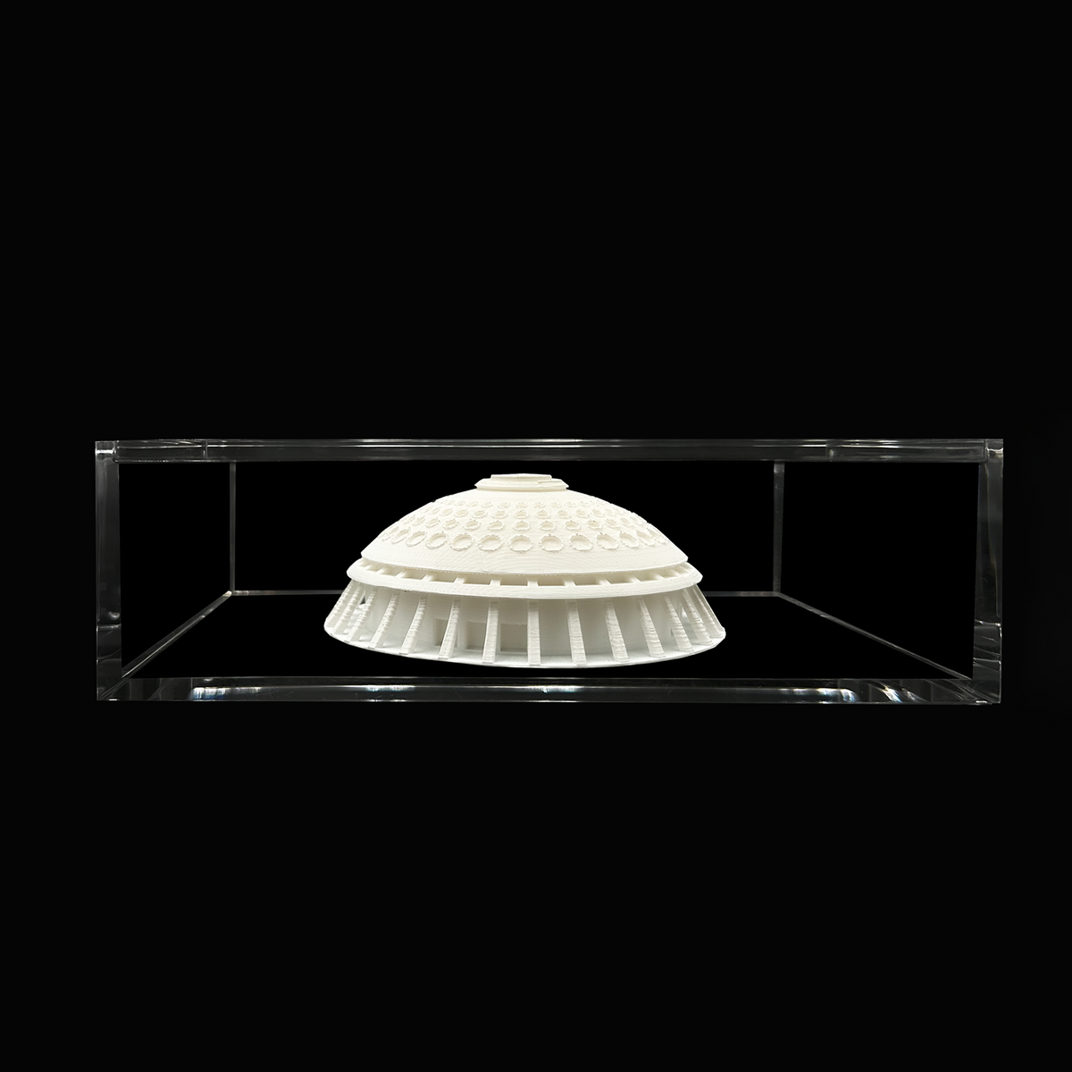 A white, dome-shaped object is displayed in a clear glass case against a black background.