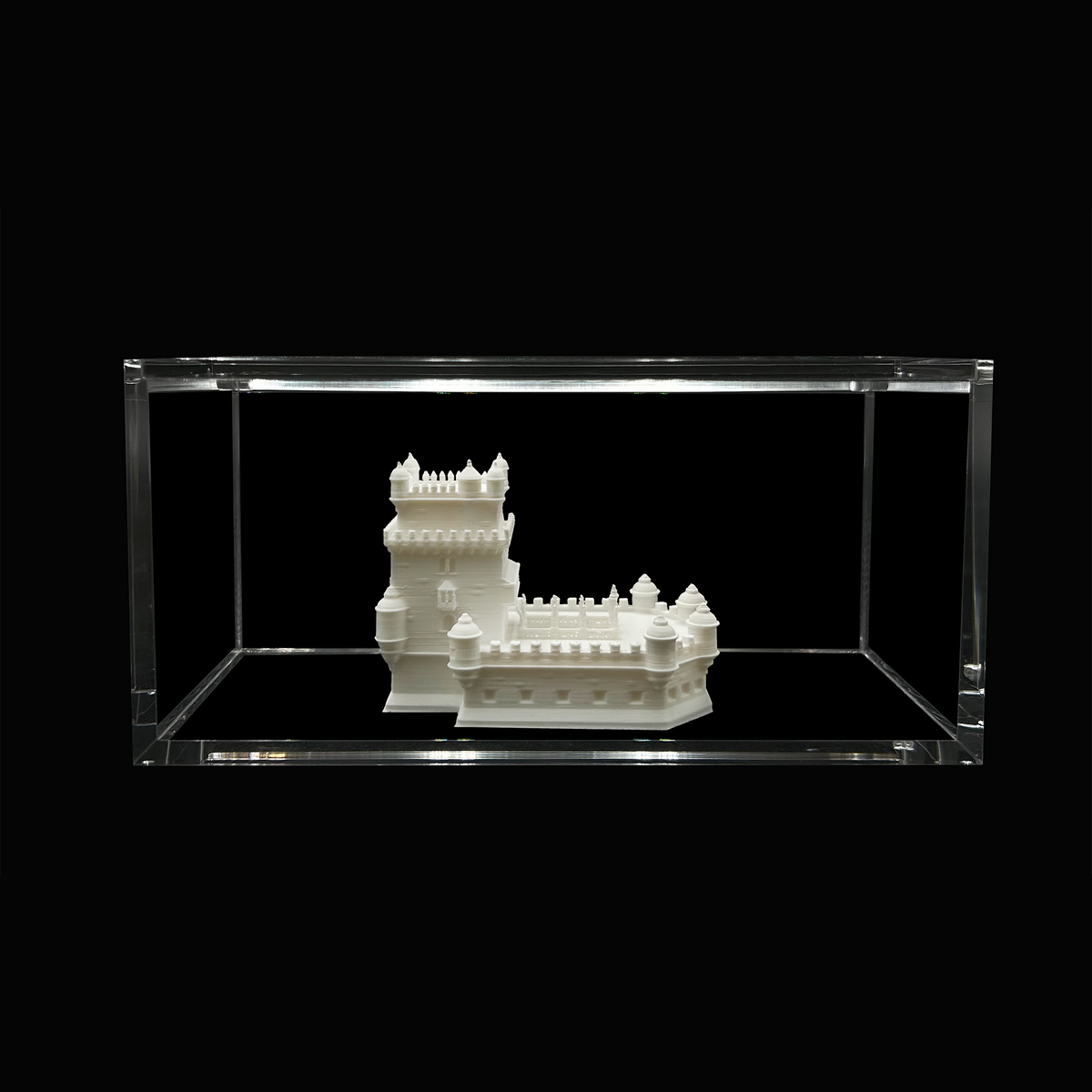 A white 3D model of a castle is displayed in a clear glass case against a black background.