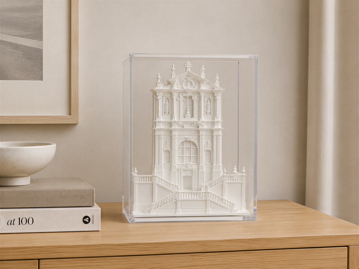 a white miniature model of a building, displayed in a clear glass case on a wooden surface.