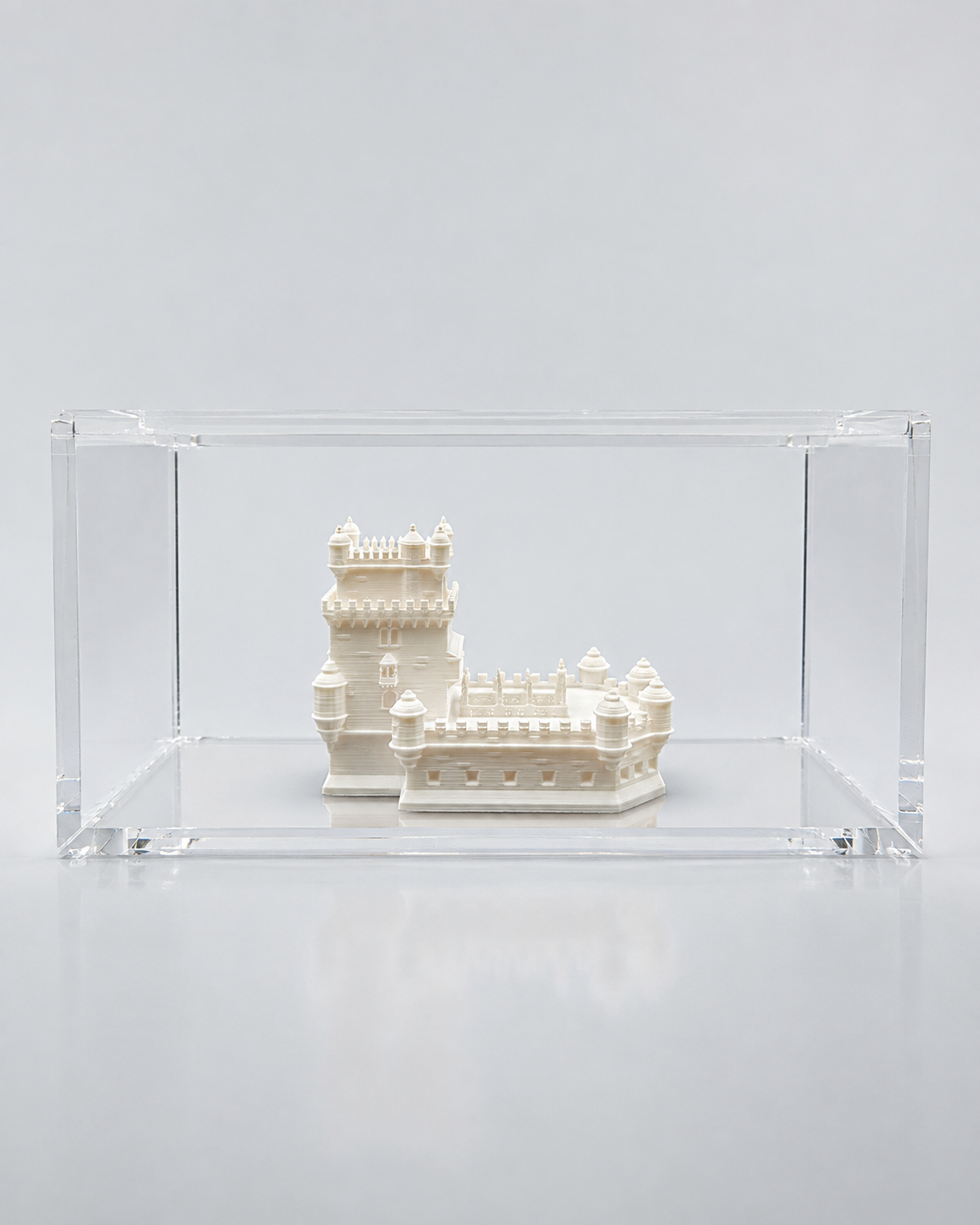 A small white castle-like structure is displayed in a clear glass case against a plain white background.
