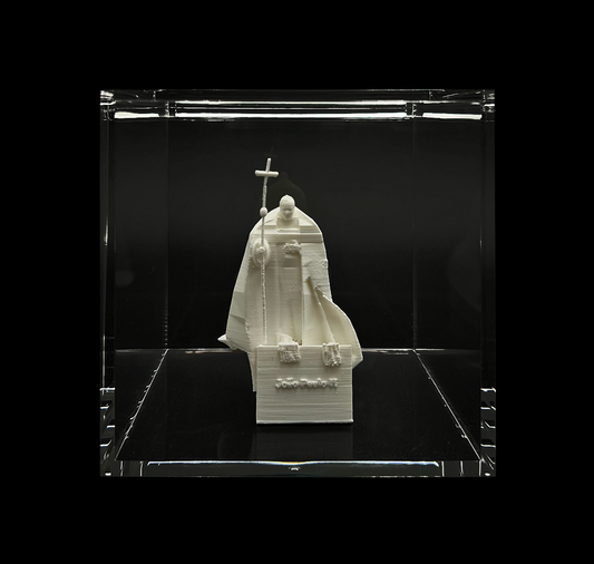 A white sculpture of a religious figure, possibly a saint or religious leader, displayed in a glass case against a black background.