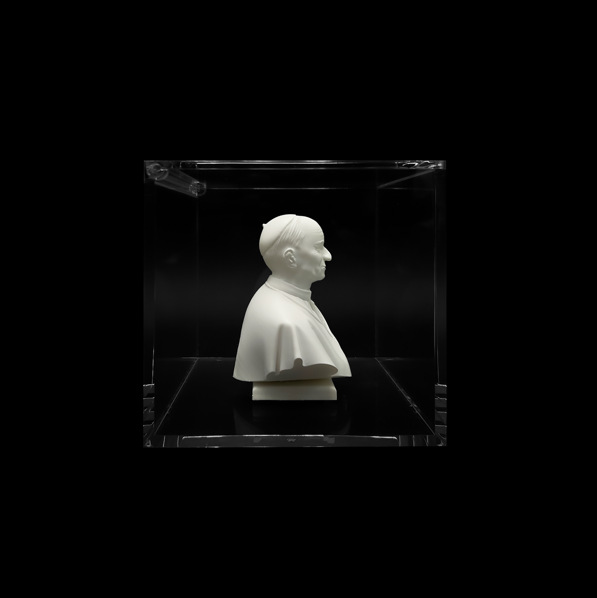 A white bust of a person is displayed in a clear glass case against a black background.