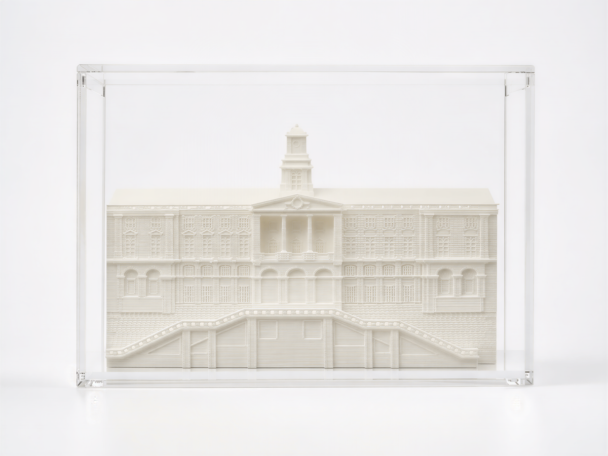 A white, three-dimensional model of a building with a tower, displayed in a clear glass case.