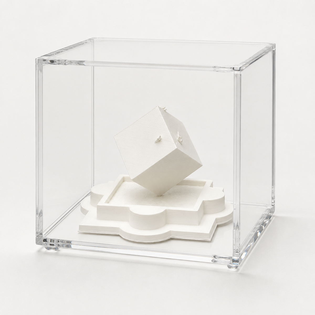 A white cube-shaped object is displayed in a clear glass case, which is placed on a white surface.
