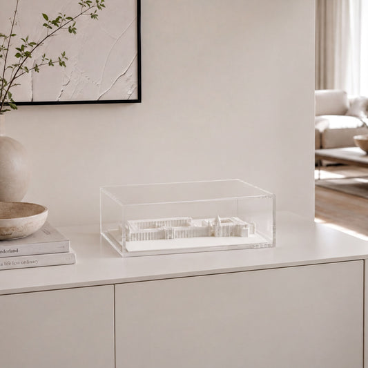 a minimalist interior design with a white dresser, a clear glass box containing a model of a building, and a framed artwork on the wall.