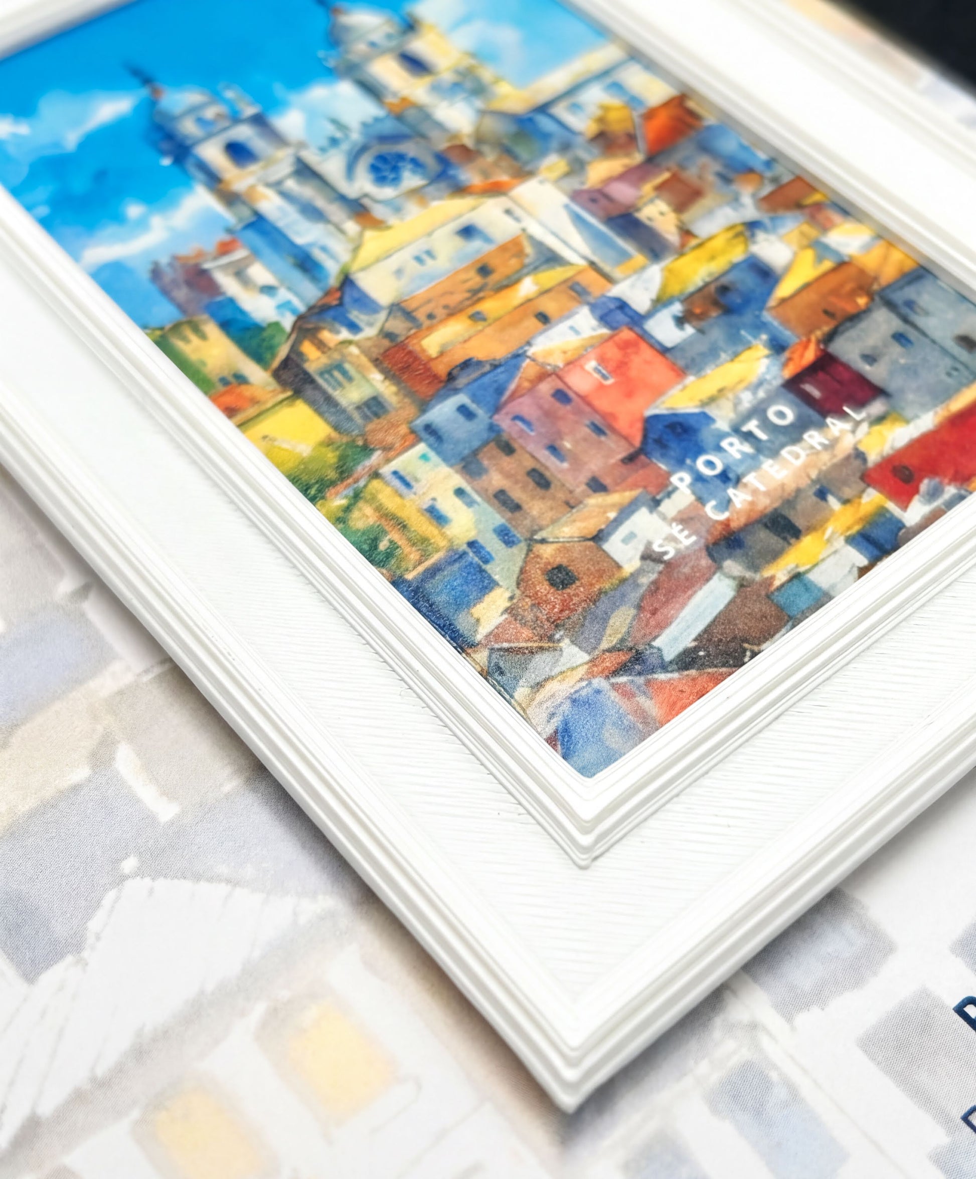 The image is a framed painting depicting a colorful and vibrant cityscape, with buildings and structures in various shades of blue, yellow, and red.