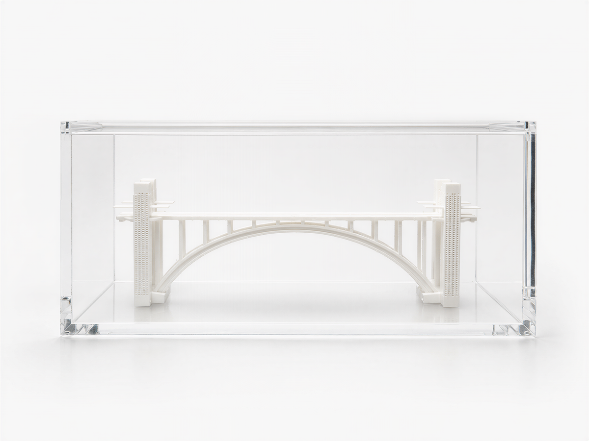 A small white bridge model is displayed in a clear glass case.