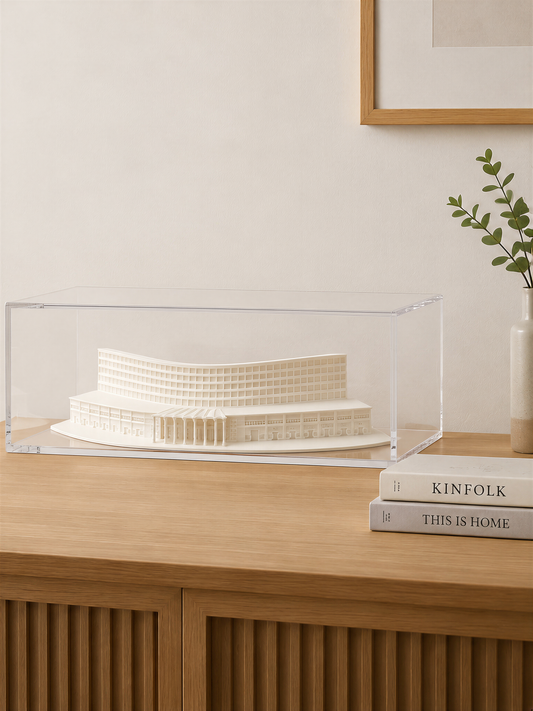 a wooden cabinet with a clear glass display case containing a white model of a building, and a stack of books titled "Kinfolk" and "THIS IS HOME" on top of the cabinet.