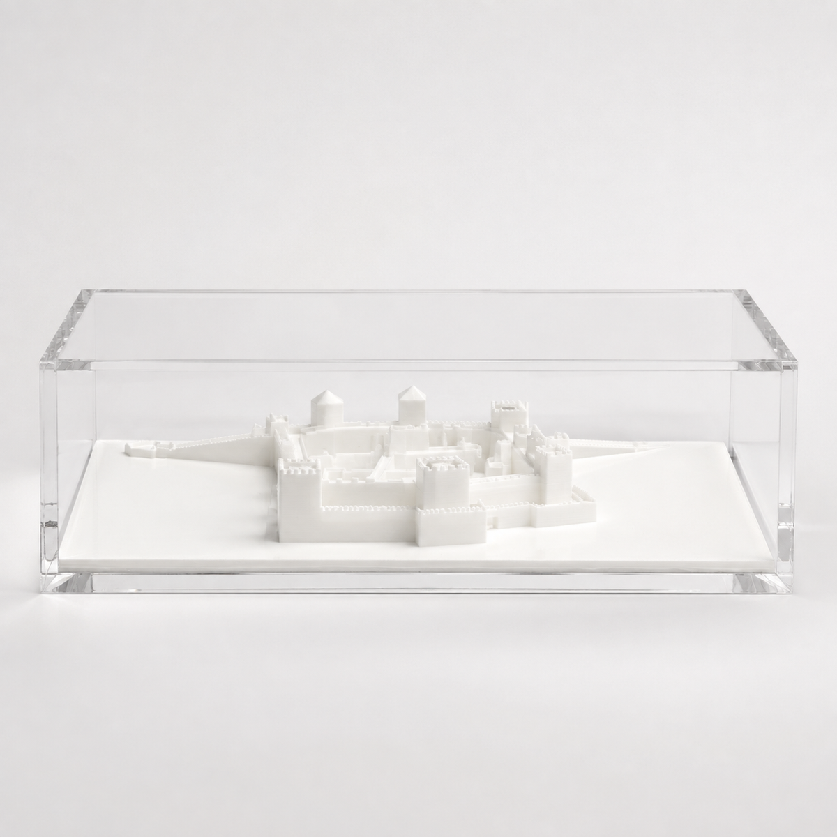 A white, three-dimensional model of a castle or fortress displayed in a clear, rectangular glass case.
