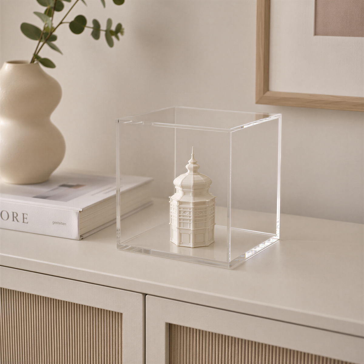 a small white ceramic model of a building, displayed in a clear glass case on a white surface.