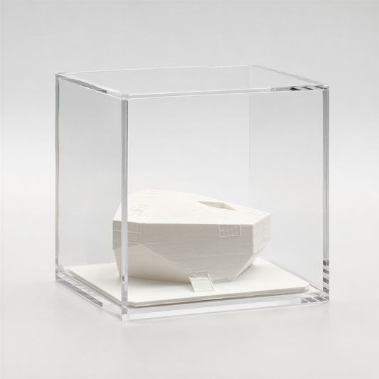 A white, three-dimensional sculpture is displayed in a clear glass case, which is placed on a white surface.