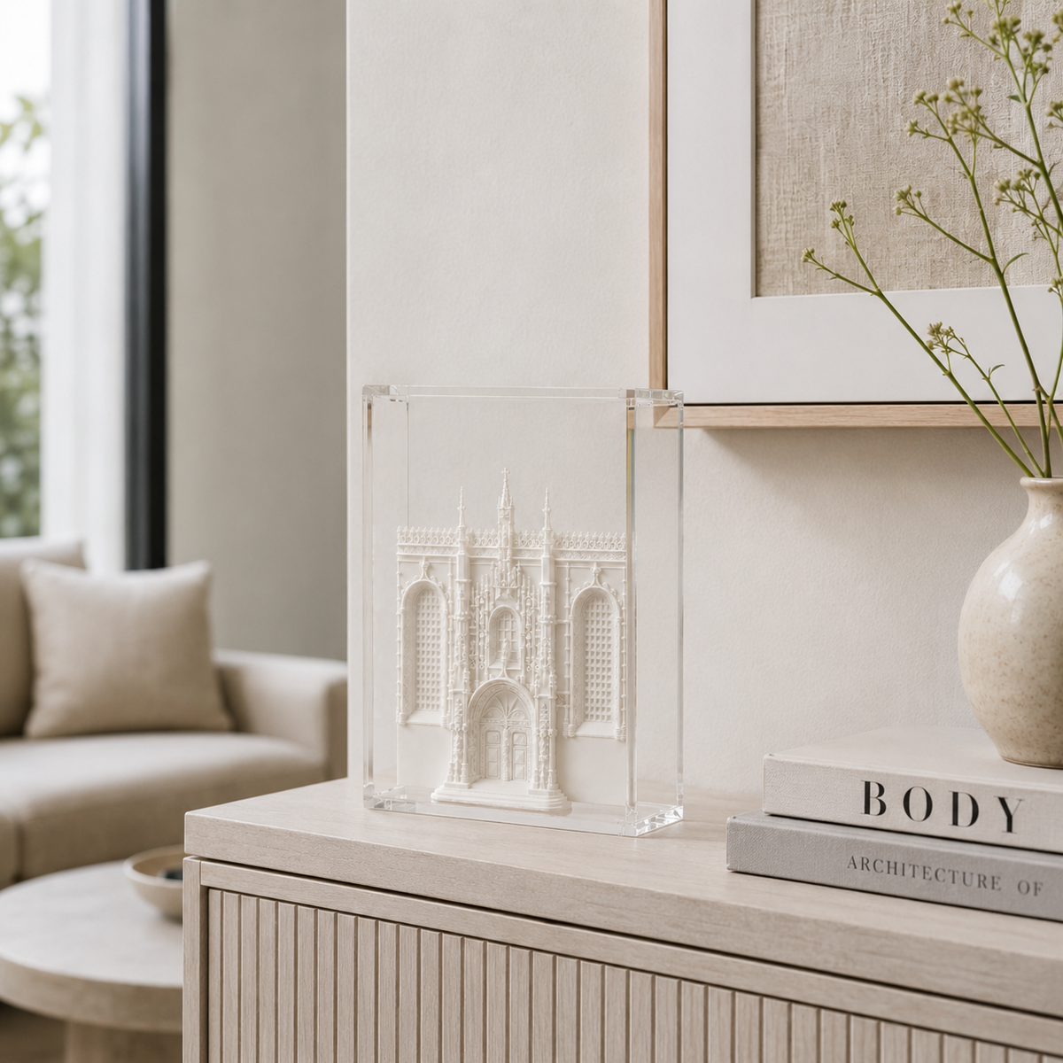 a living room with a beige sofa, a glass display case containing a miniature model of a building, and a book titled "BODY ARCHITECTURE OF".