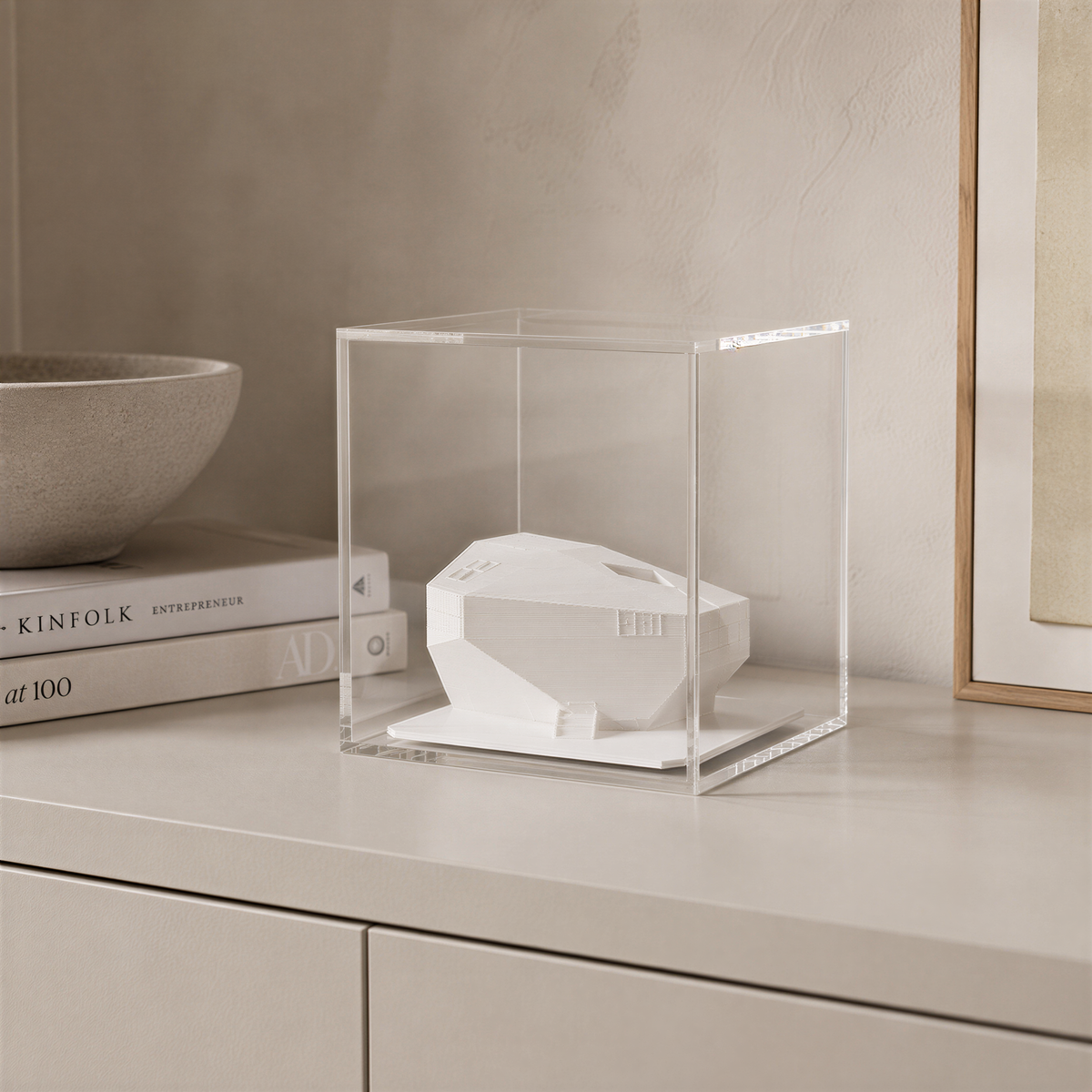 a white ceramic object, possibly a sculpture or a piece of art, displayed in a clear glass case on a white surface.