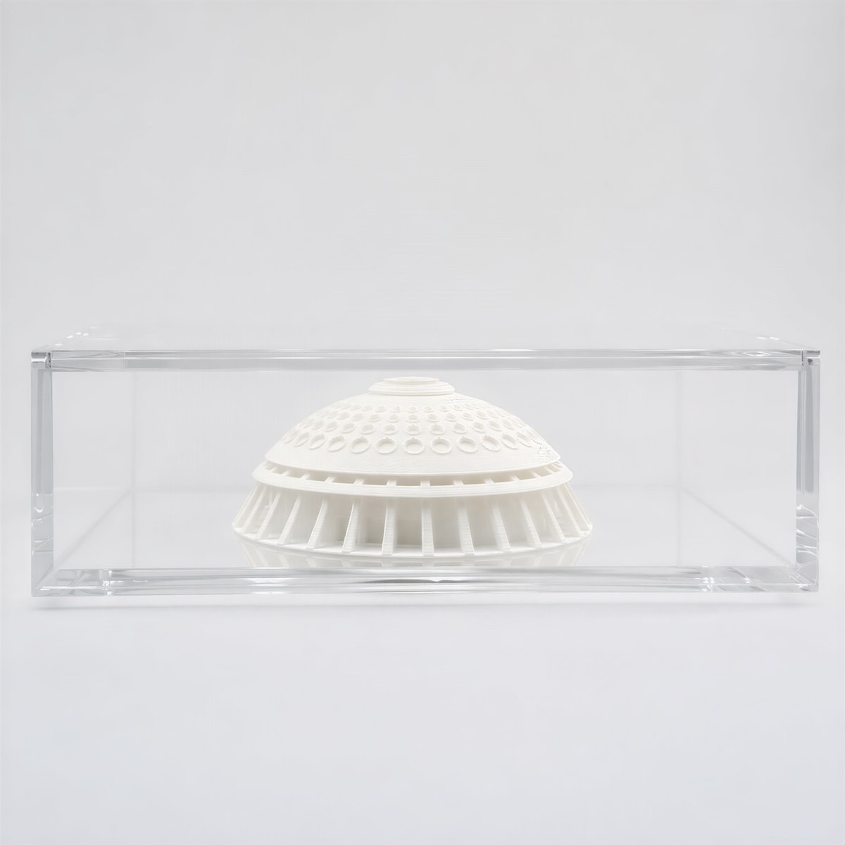A white ceramic dome or bowl is displayed in a clear glass case against a plain white background.