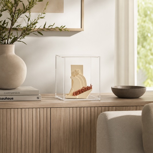 a wooden cabinet with a clear glass display case containing a small sculpture, a stack of books, a vase with greenery, and a bowl on a table.