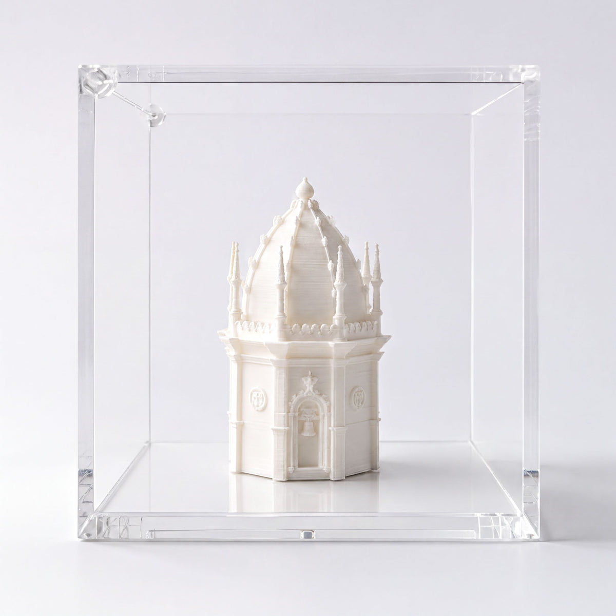 A small white ceramic tower or building is displayed in a clear glass case against a plain white background.