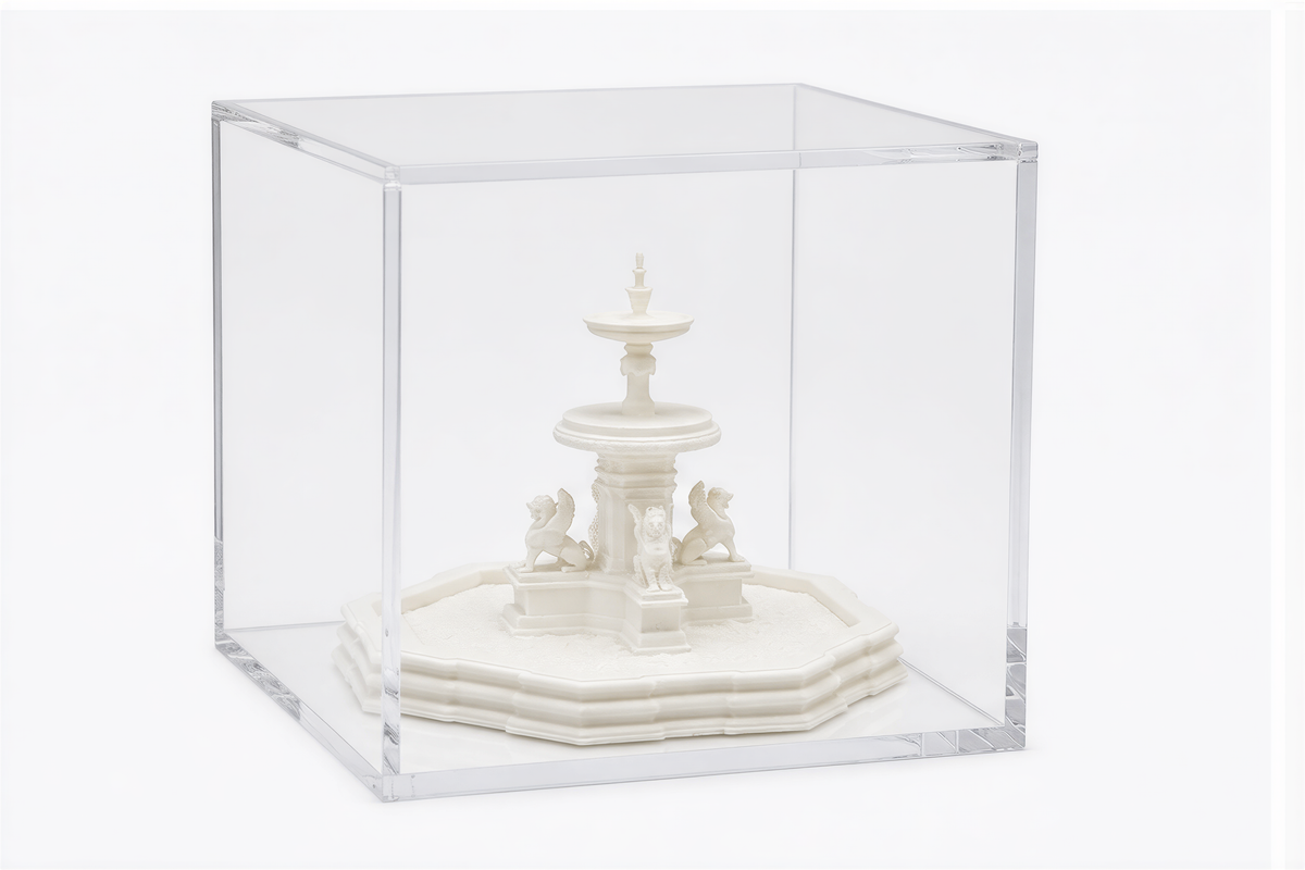 A white ceramic fountain with a small statue of a lion is displayed in a clear glass case.