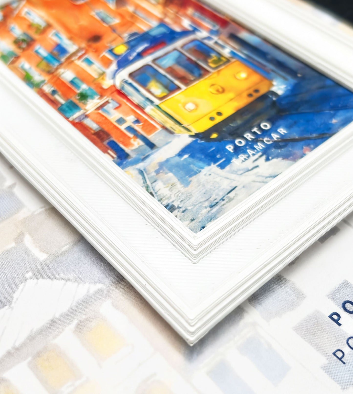 a framed painting of a yellow tram in a city setting, with a blurred background that appears to be a cityscape.