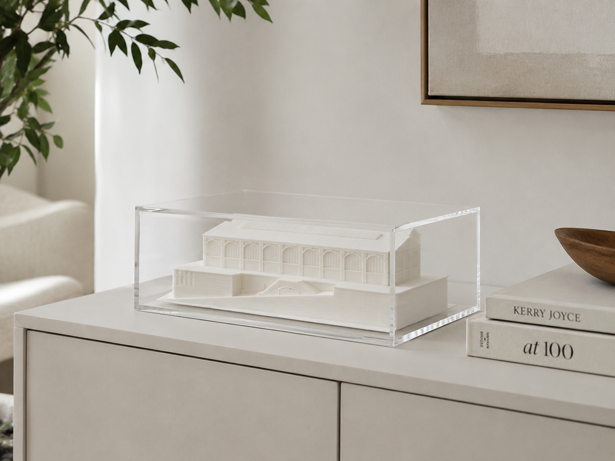 a white architectural model displayed in a clear glass case on a white dresser.