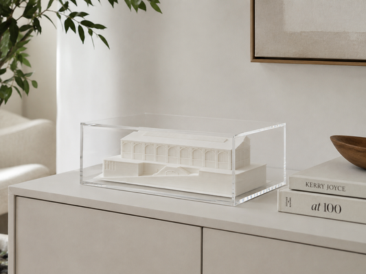 a white architectural model displayed in a clear glass case on a white dresser.
