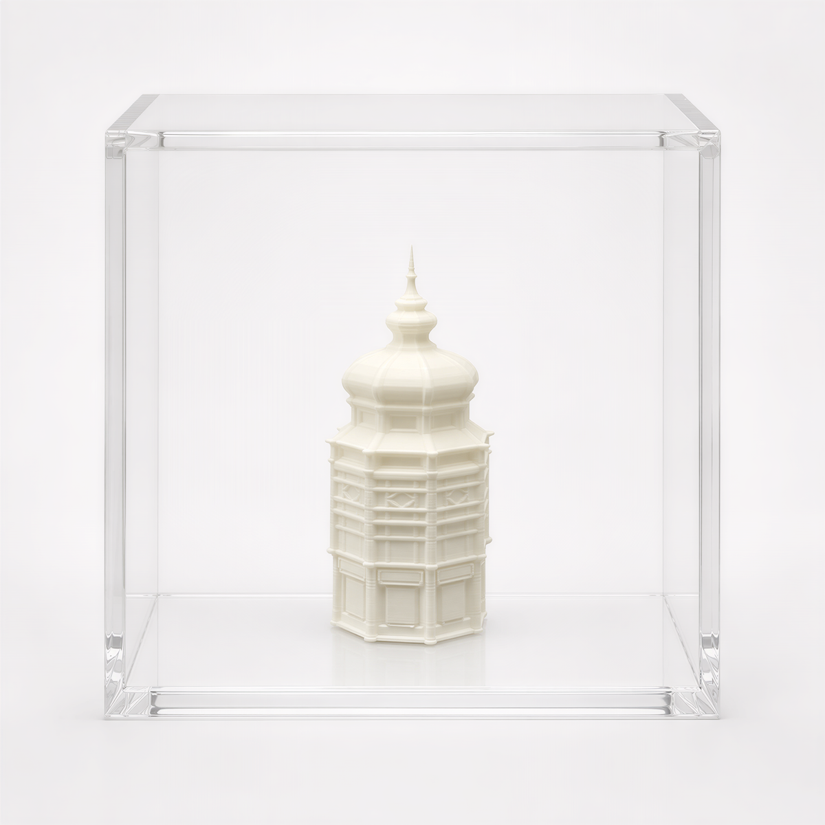 A small white ceramic tower or building is displayed in a clear glass case against a white background.