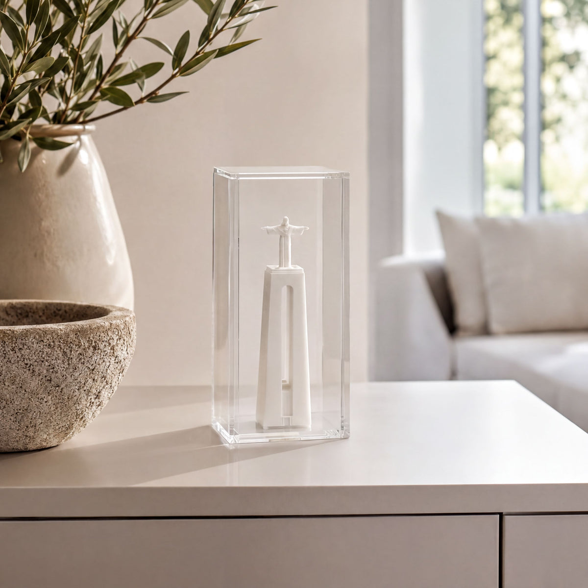 a small white sculpture of a person inside a clear glass case, placed on a white surface.