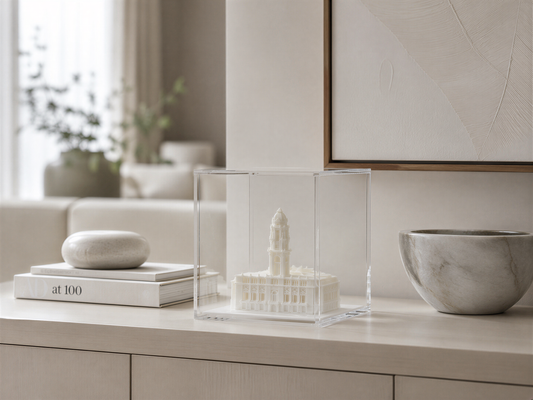 a minimalist living space with a clear glass display case containing a miniature model of a building, a marble bowl, and a stack of books.