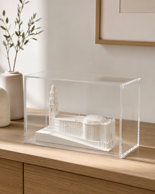 A clear glass display case containing a miniature model of a building, placed on a wooden surface.