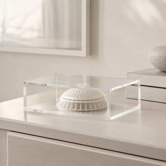 A clear glass display case containing a white ceramic object, possibly a decorative piece or a figurine, sits on a wooden surface.