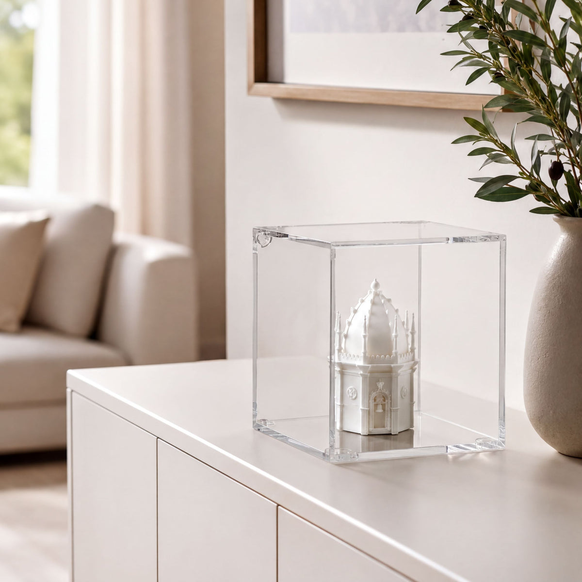 A small white model of a building, possibly a castle or cathedral, is displayed in a clear glass case on a white cabinet or dresser.