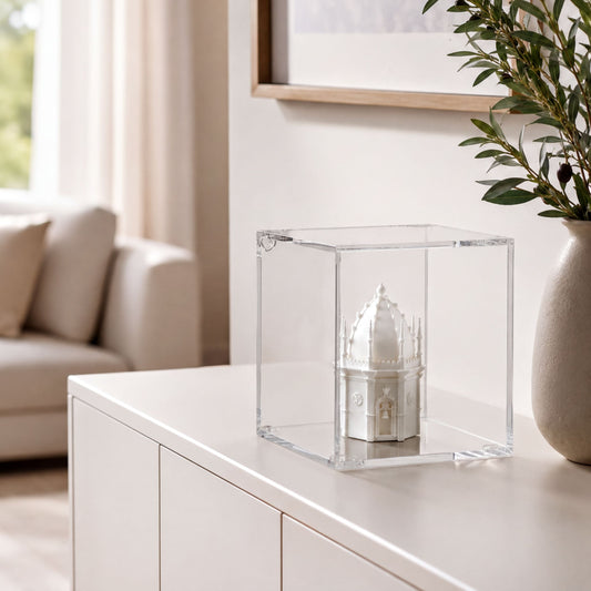 A small white model of a building, possibly a castle or cathedral, is displayed in a clear glass case on a white cabinet or dresser.