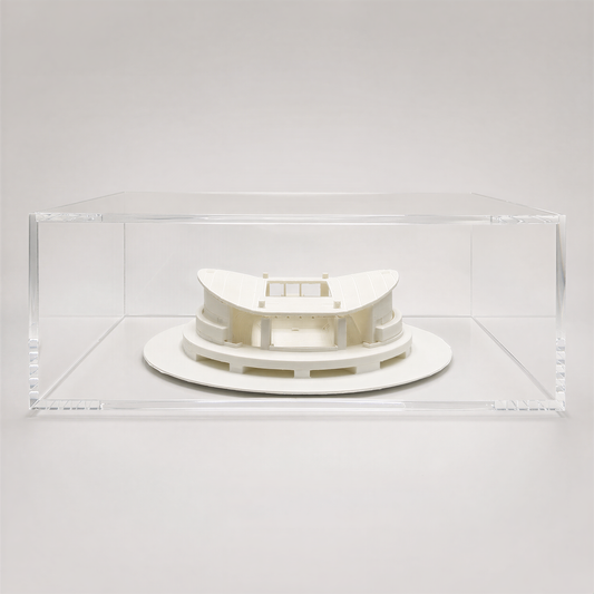 A white, circular model of a building or structure is displayed in a clear, rectangular glass case.