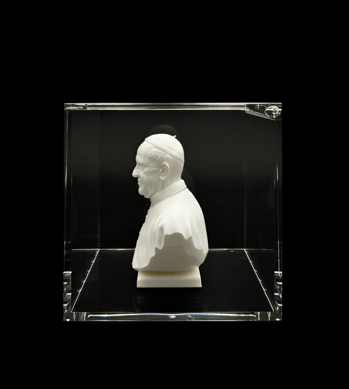 A white bust of a person is displayed in a clear glass case against a black background.