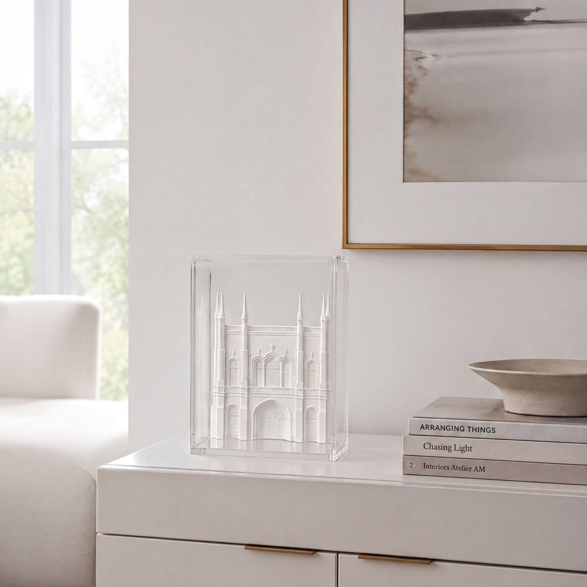 a white dresser with a clear glass box containing a miniature model of a building, placed on top of a stack of books.