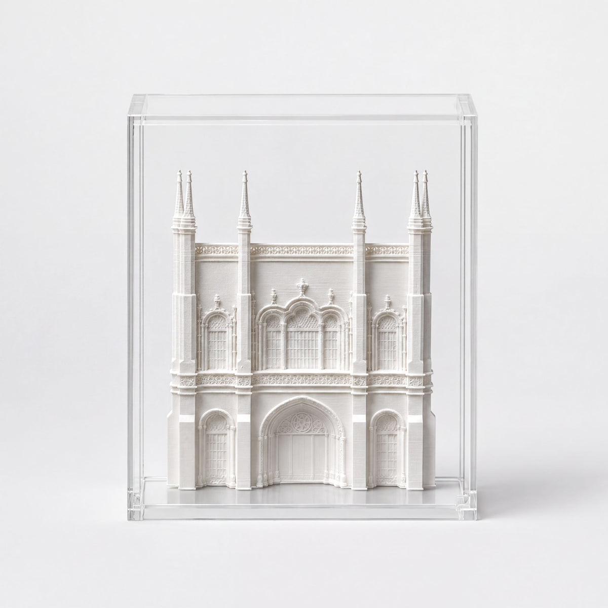 A white miniature model of a building, possibly a castle or cathedral, displayed in a clear glass case.
