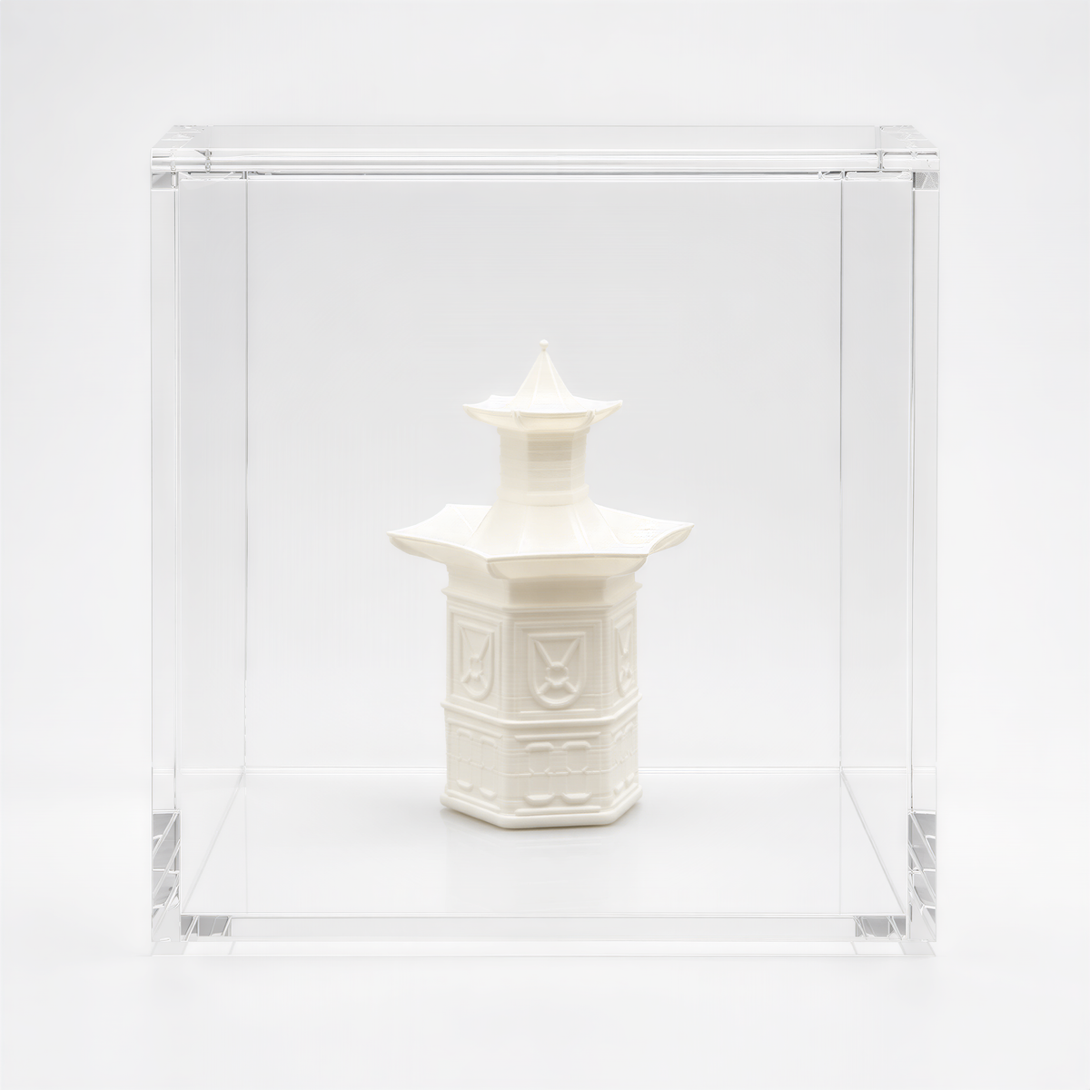 A white ceramic object, possibly a vase or sculpture, is displayed in a clear glass case against a white background.
